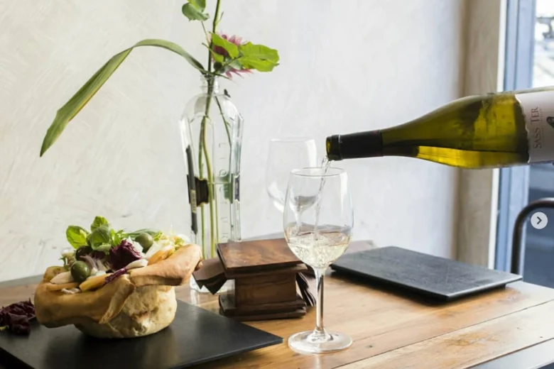 Calice di vino bianco versato a tavola accanto a pane ripieno e decorazioni floreali