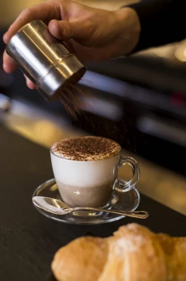 Barista che spolvera cacao su cappuccino artigianale