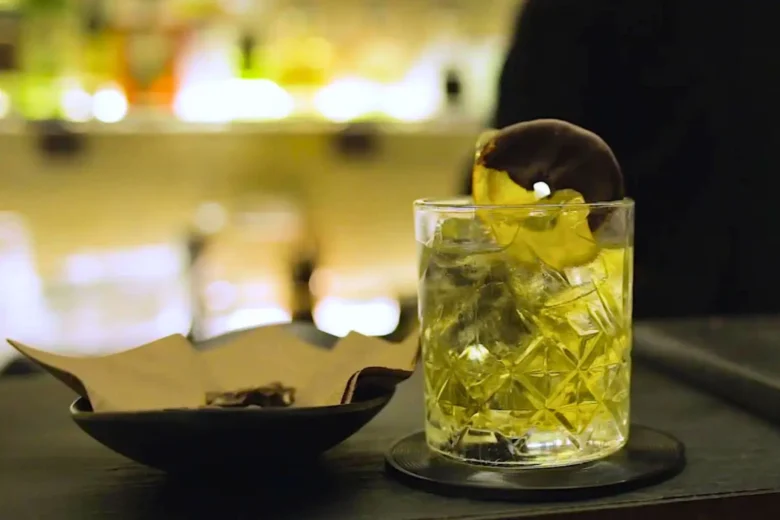 Cocktail giallo servito con ghiaccio e guarnizione al cioccolato in un bicchiere basso