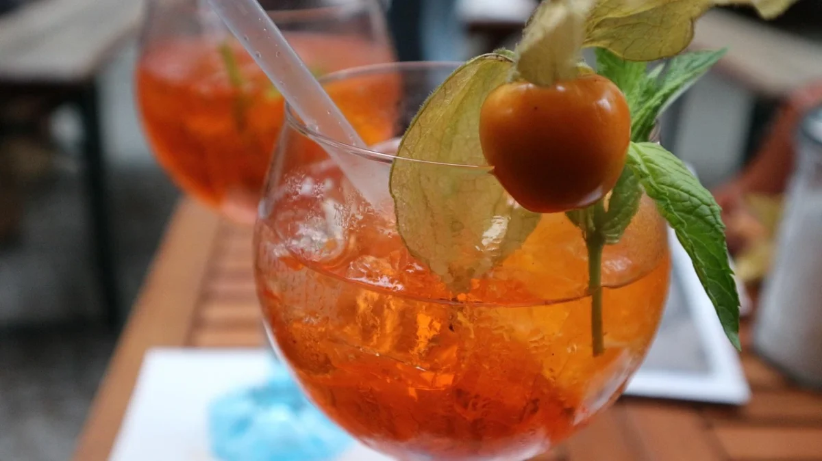 Calice di Spritz con oliva e fetta d’arancia su tavolino da aperitivo.