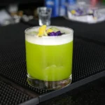 Cocktail verde in bicchiere lowball con schiuma e fiori edibili