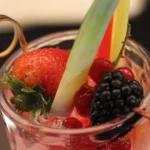 Cocktail analcolico decorato con fragola, mora, ribes rosso e fetta di ananas.