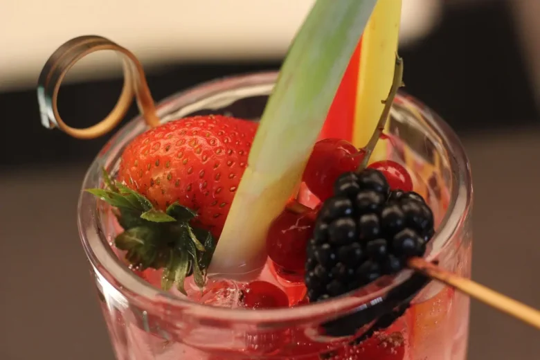 Cocktail analcolico decorato con fragola, mora, ribes rosso e fetta di ananas.